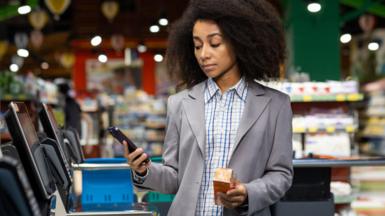 Unimpressed woman at self-checkout till paying for item using her phone