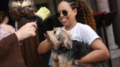 A woman holds a mid-size dog up to be blessed with holy water.