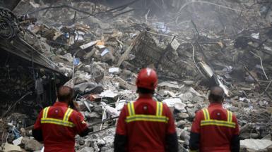 Search and rescue officials stand before a site in Tehran heavily damaged by airstrikes