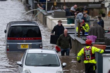 Residents stand in floodwater in Wales, using buckets to bail it away from their homes. Cars can also be seen submerged in the water