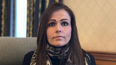 Lucy Domaille - a woman with long brown hair, looking at the camera. She is wearing a leopard print scarf with a black jumper underneath. 