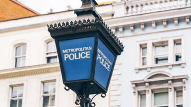 A blue Metropolitan Police lamp post with the words Metropolitan Police in white writing. There's a white building in the background 