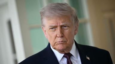 A picture of US President Donald Trump wearing a white shirt, navy suit and blue and red spotted tie.