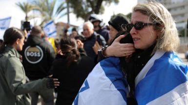 Women wearing the Israeli flag around their shoulders embrace in anguish as the convoy transporting the bodies of deceased hostages, identified at the time by Hamas as Oded Lifschitz, Shiri Bibas and her two children Kfir and Ariel Bibas arrived in Tel Aviv