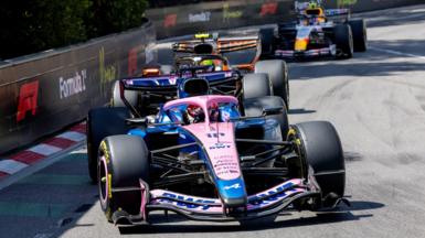 Alpine's Pierre Gasly with McLaren's Lando Norris right behind him, and a Racing Bulls in the background, approaching the hairpin during the Monaco Grand Prix