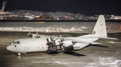 A Royal Danish Air Force Lockheed C-130J Super Hercules aircraft vehicle is parked on the tarmac at Nuuk international airport, Greenland. Snow has been cleared from the tarmac and is piled in an area behind the plane.. 