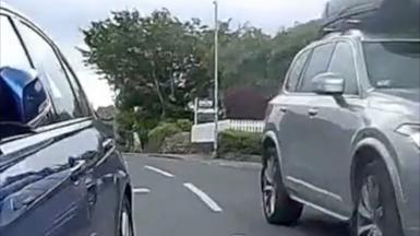 The view from a cyclist's camera as they weave between a parked car on the left and an oncoming vehicle on the right