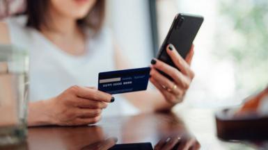 A woman is holding a credit card or debit card and doing online shopping on a smartphone. 