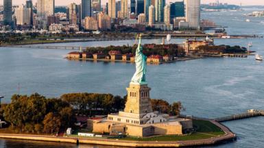 aerial shot of Statue of Liberty and waters surrounding it with New York skyline in background