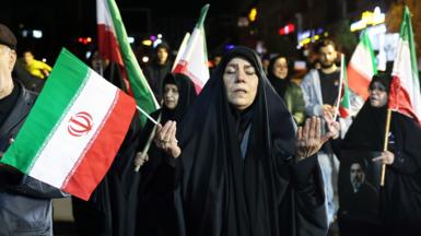 A woman holding an Iranian flag and praying on a protest in support of Iran's supreme leader Mojtaba Khamenei in Tehran, March 25th