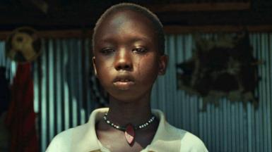 A tear rolls down the face of Michelle Lemuya Ikeny as she plays the character of 13-year-old girl Nawi. She has close cropped hair, wear a pale yellow shirt and a bead necklace around her neck