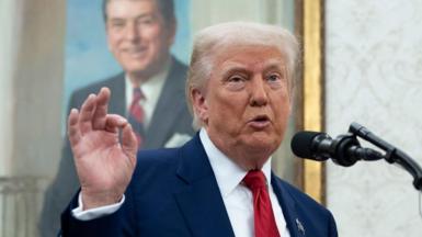 Donald Trump holds his index finger and his thumb together, as he speaks into a microphone in the White House. A portrait painting is behind him.