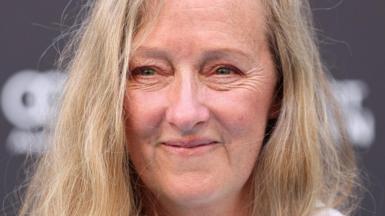 A close up of a middle-aged woman with long blonde hair, smiling at the camera.