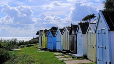 A row of colourful beach huts under a bright but cloud-filled sky