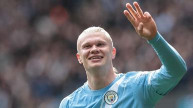 Erling Haaland, wearing Manchester City's light blue kit, celebrates his latest hat-trick by making a three-finger salute with his left hand