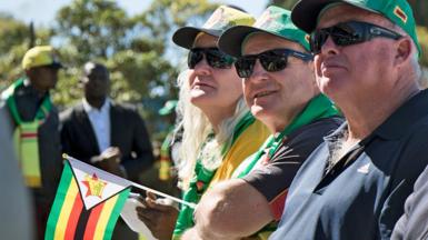 Two men and one woman in green hats and one holding a Zimbabwean flag attend a political campaign meeting held by President Emmerson Mnangagwa in July 2018 for members of the white farming and business community.