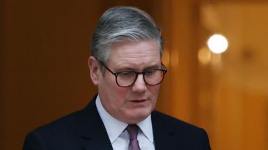 Sir Keir Starmer wearing dark suit and glasses looks down at floor