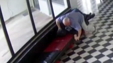 A still from CCTV footage showing a male in light coloured clothing lunging towards another male in dark clothing.