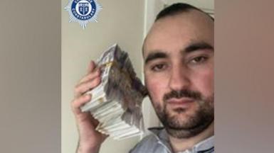 A man is holding a bundle of cash next to his head 