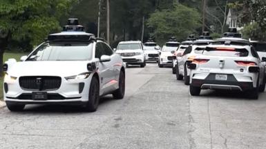 A litany of Waymo cars take up all the space in a street.