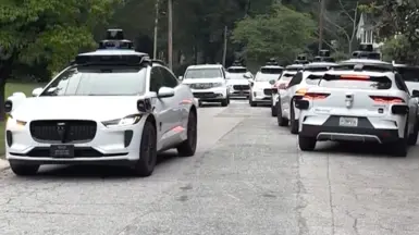 A litany of Waymo cars take up all the space in a street.