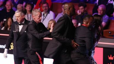 A female spectator (right) is escorted out of the arena at the Crucible Theatre in Sheffield after jumping the barrier between the seats and the playing area