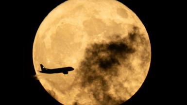A plane flies in front of the full Moon