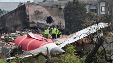 The aftermath of the Air India crash showing a part of the plane crashed in the ground. Three men in high-vis jackets inspect the sight. Taken on 15th June 2025.