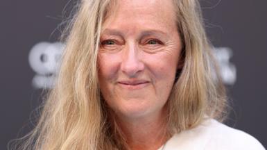 A close up of a middle-aged woman with long blonde hair, smiling at the camera.