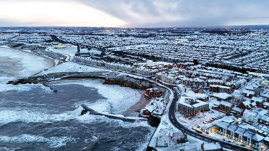 An aerial view of Cullercoats Bay in North Tyneside, showing houses covered in snow and frost along the coast.