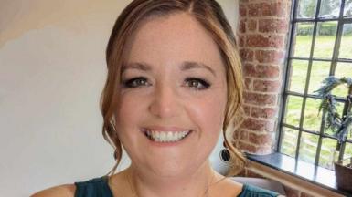 Ellie Lambert wears her hair in a wavy up do and wears pendant earrings as she beams in a selfie while attending an event  