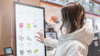 A woman touches the screen of a self-service terminal at a fast-food restaurant