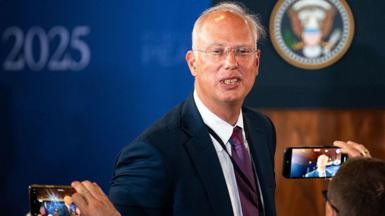 Kirill Dmitriev in a blue jacket poses for photographers in Alaska with whispy silver hair and transparent glasses