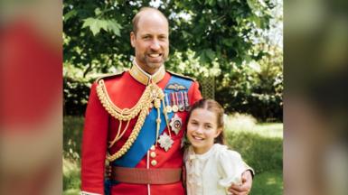 Prince William is wearing the scarlet dress uniform of the Welsh Guards, of which he is colonel, and has his arm around Charlotte, who is wearing a cream dress.