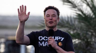 Elon Musk waving towards the camera wearing a T shirt with the slogan Occupy Mars