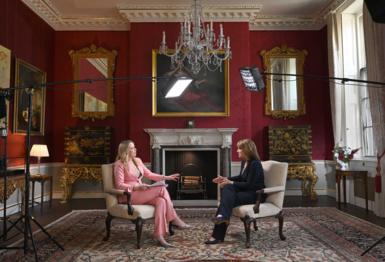 Rachel Reeves on the right, in a blue suit, being interviewed by Laura Kuenssberg on the left, in a pink suit, in a grand room underneath a large chandelier