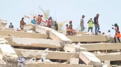 A landscape image of people conducting a search on top of a mass of rubble from collapsed buildings