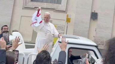 Pope Leo waves the jersey from the pope-mobile