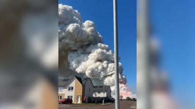Mobile phone footage of large plumes of smoke and flames rising behind new build homes.