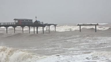 Teignmouth Pier crumbling into the sea during Storm Ingrid. The waves are grey and lashing the pier, which has become damaged.