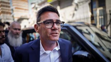 Image shows Andy Burnham wearing black-rimmed glasses and a blue suit, arriving at the Houses of Parliament in Westminster, London, Britain, on 22 June 2026