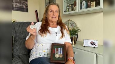 Angie Moore, with long brown hair, is pictured holding her son's dog tags and Afghanistan medals