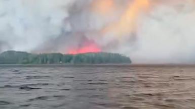 Smoke and flare behind a forest, seen from afar in the ocean.
