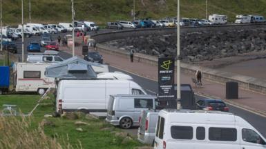 Motorhomes parked along a road on Scarborough’s North Bay with a wide pavement on the right hand side overlooking a beach with rocks in the background.
