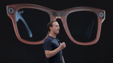 Meta CEO Mark Zuckerberg on a stage describing Meta's Ray-Bans, a large image of which is being shown behind him.
