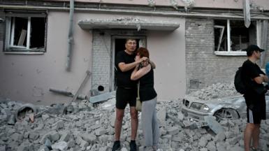 Couple stands at the foot of building strewn with debris