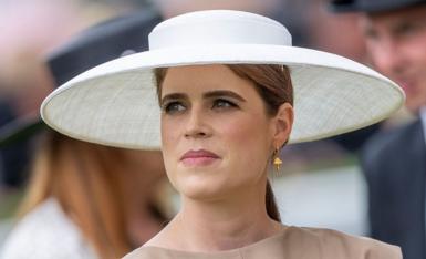 Princess Eugenie wearing a large wide-brimmed white hat, gold toadstool earring and brown dress