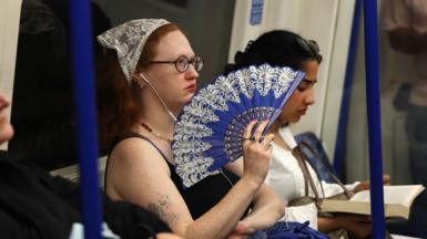 A woman with a bandana holding a blue fan sitting on the London underground