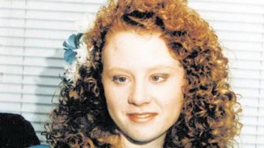 A family image of a young girl, dressed for a wedding in a bridesmaid's dress in blue, with curly red hair and blue and white flowers in her hair.