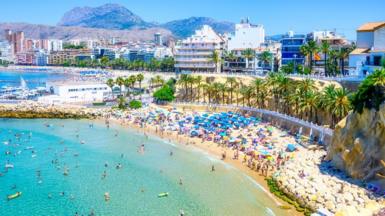 Beach in Benidorm, Spain. The sky is deep blue, there are palm trees and hotels in the background and people swimming in the sea